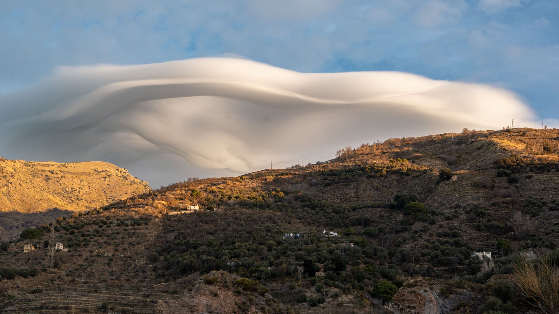 A large lens type cloud known as a lenticular is above a morning mountainside. A sign of high winds at altitude