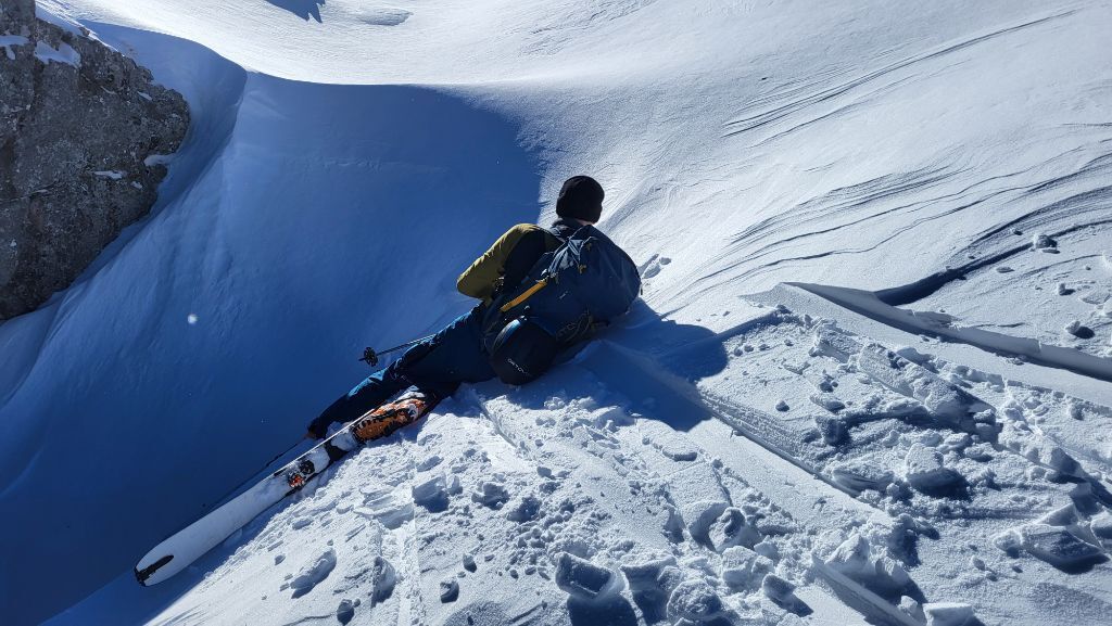 A Person with touring ski laying in the snow for catching a photo.